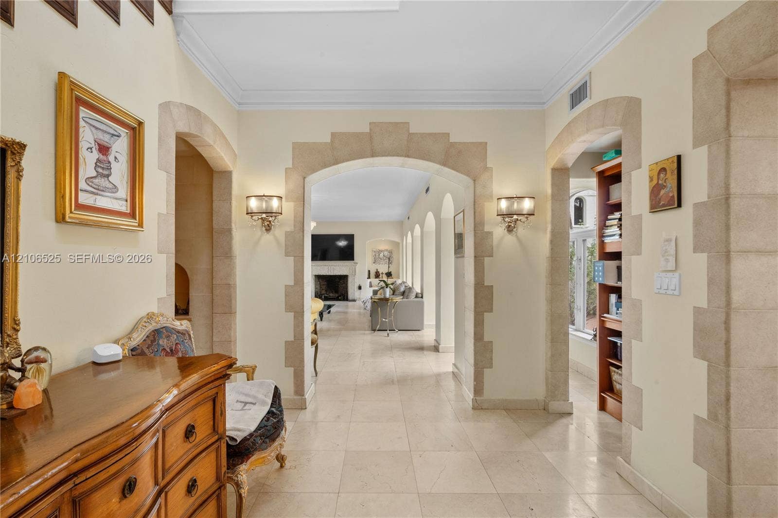4760 N Bay Road, Miami Beach, FL 33140 Foyer featuring arched stone-trimmed doorways, crown molding, stone tile flooring, and wall-mounted light fixtures