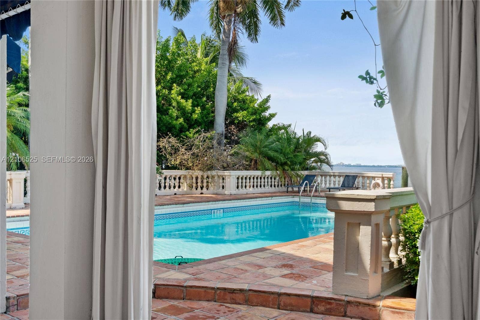 4760 N Bay Road, Miami Beach, FL 33140 Rectangular swimming pool featuring terracotta tile decking, concrete balustrade fencing, and mature palm trees