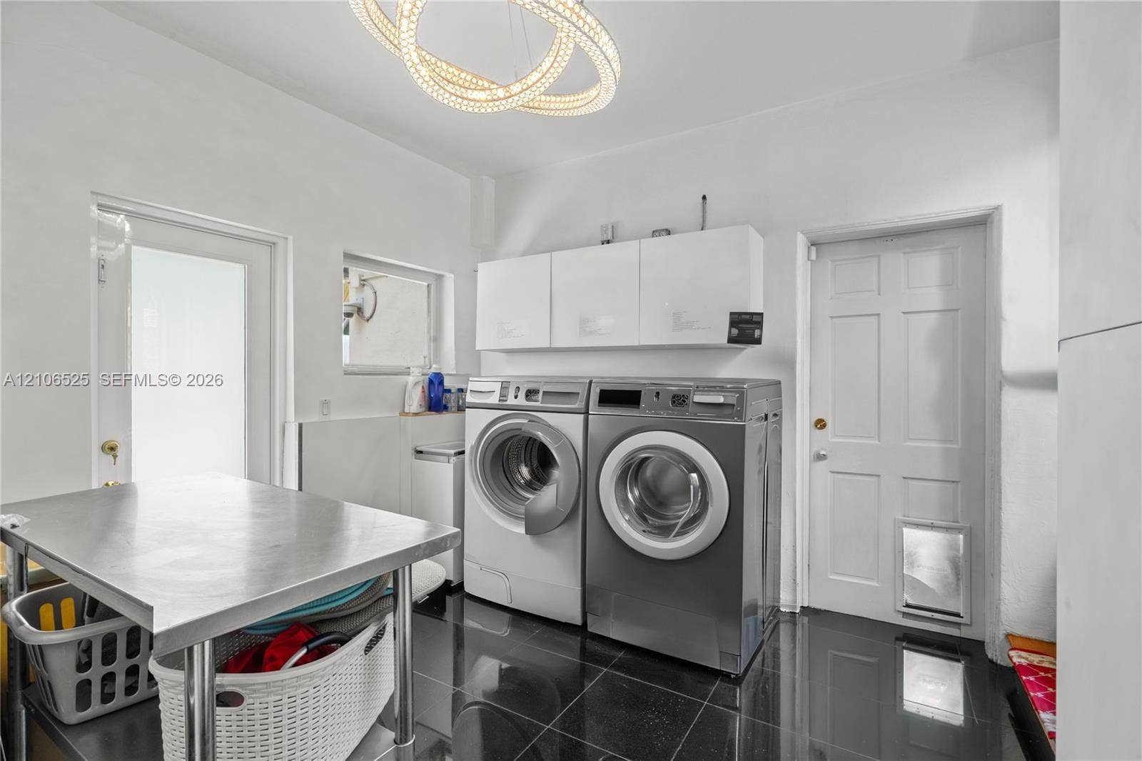 4760 N Bay Road, Miami Beach, FL 33140 Utility room featuring polished dark tile flooring, white wall-mounted storage cabinetry, a contemporary circular dual-ring chandelier, and a six-panel exterior door with a built-in pet portal