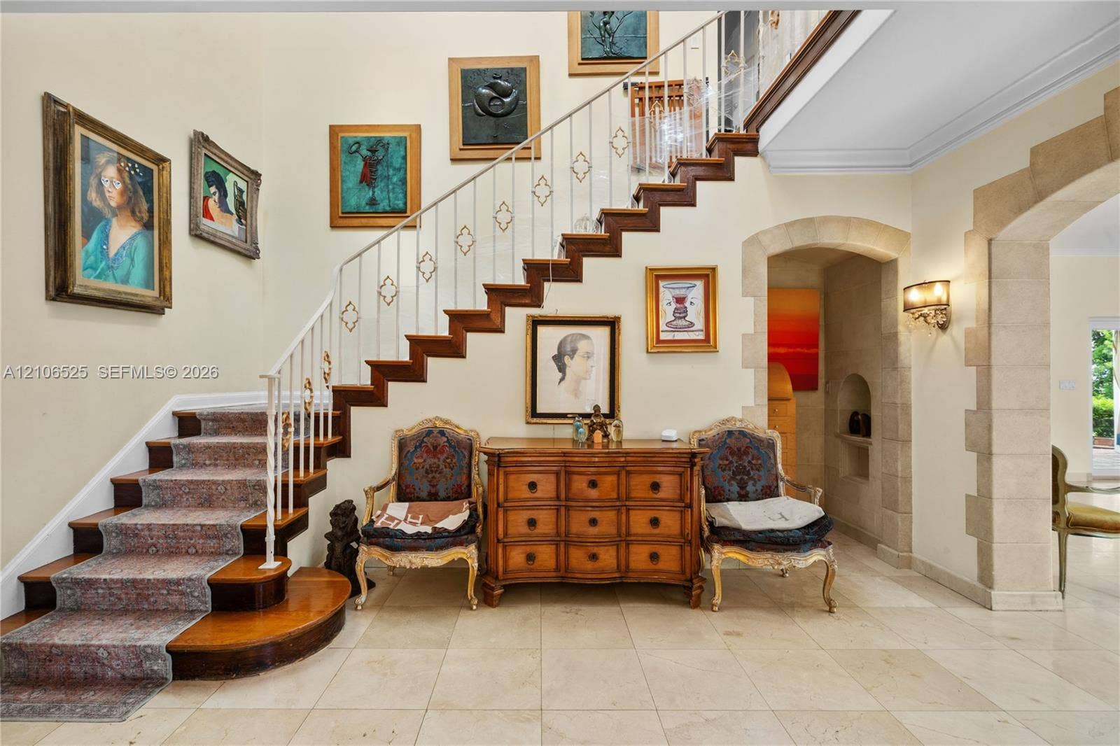 4760 N Bay Road, Miami Beach, FL 33140 Staircase featuring wood treads, ornate metal railings, and stone-tiled flooring, complemented by an arched stone-trimmed doorway