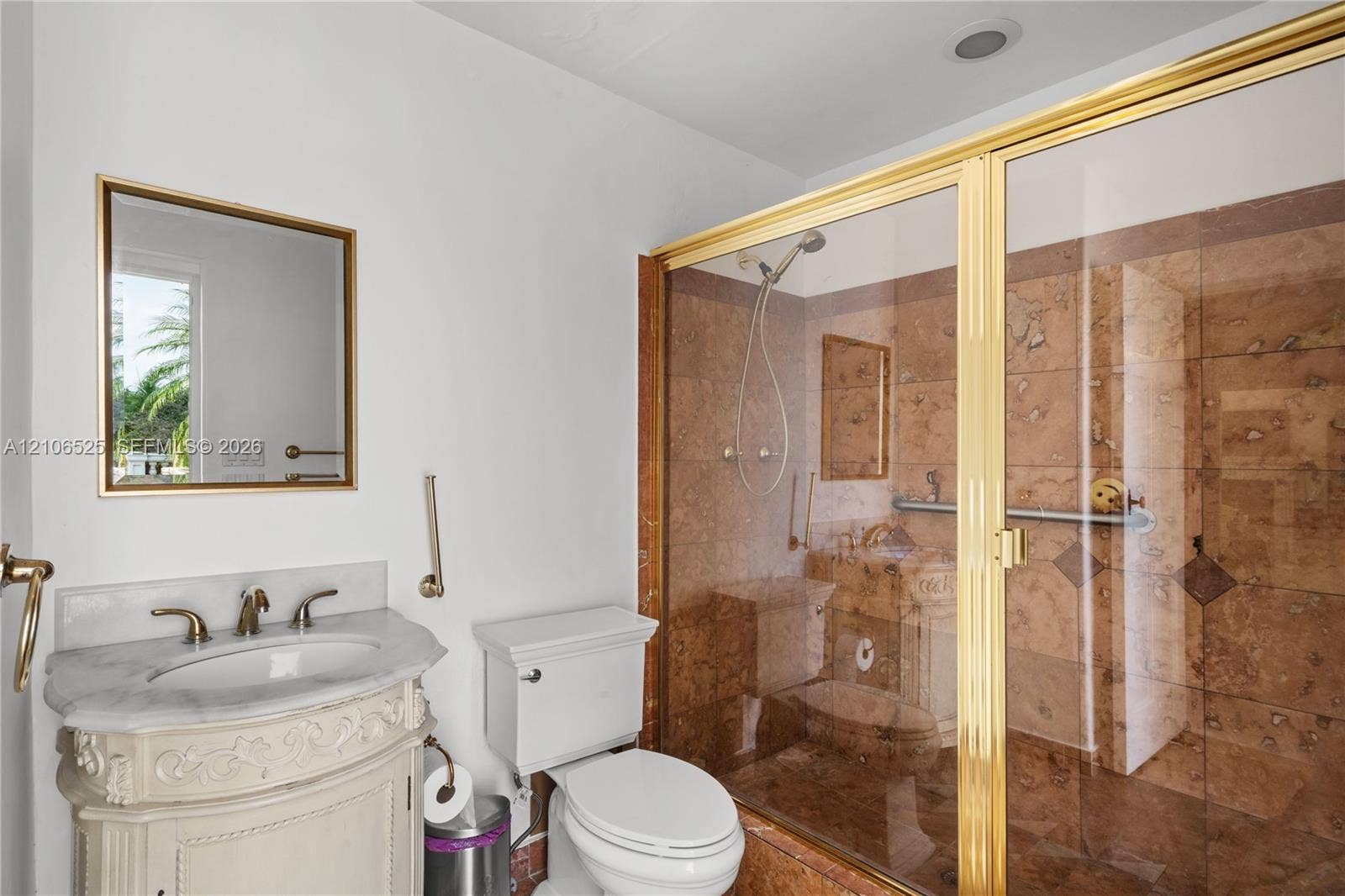 4760 N Bay Road, Miami Beach, FL 33140 Bathroom featuring a stone-topped vanity with ornate carved base, wall-mounted mirror with gold-finish frame, and walk-in shower with floor-to-ceiling stone tile surround and gold-finish enclosure