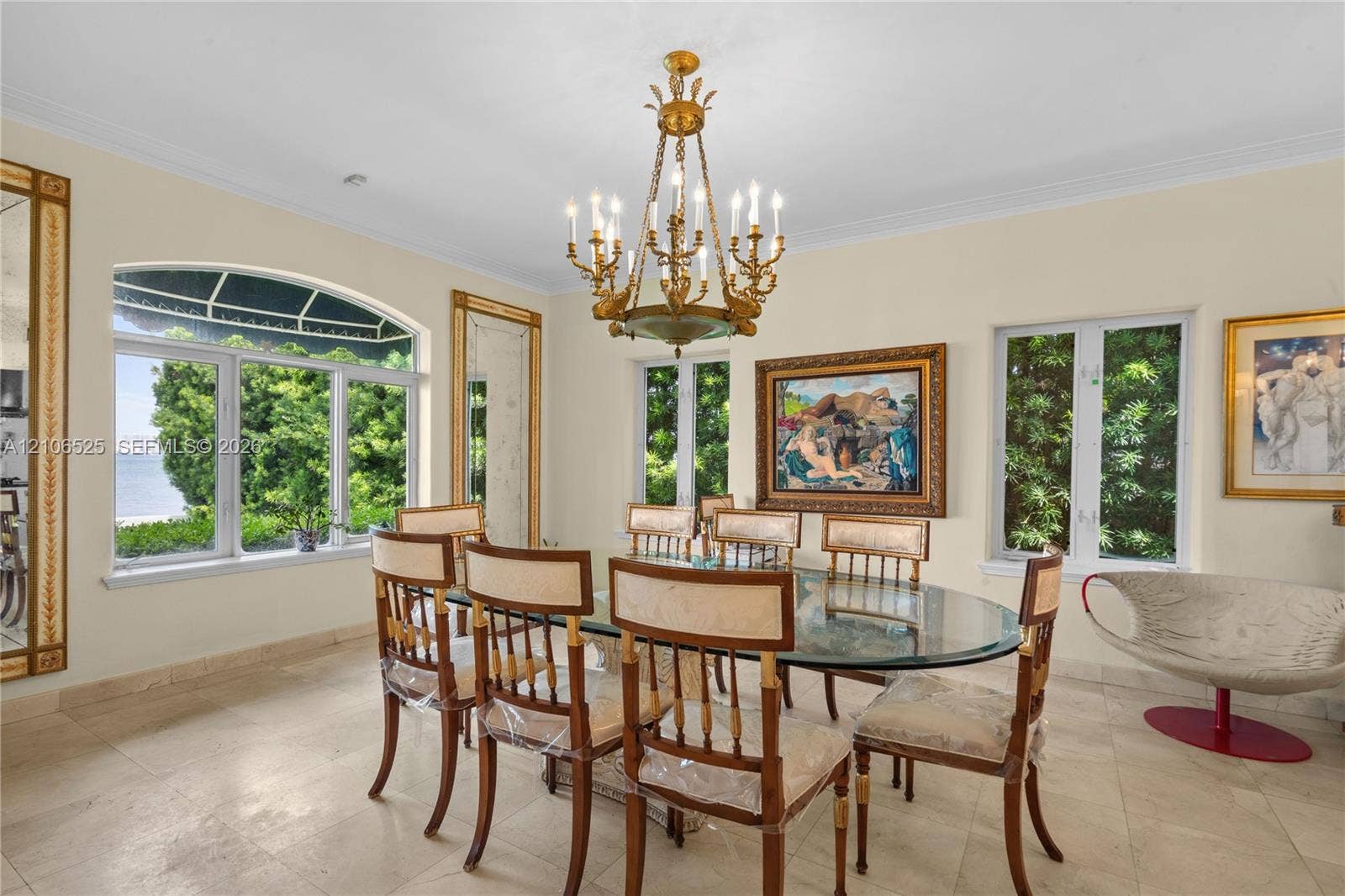 4760 N Bay Road, Miami Beach, FL 33140 Ornate brass chandelier, natural stone flooring, arched window with multi-pane glazing, and framed wall mirrors