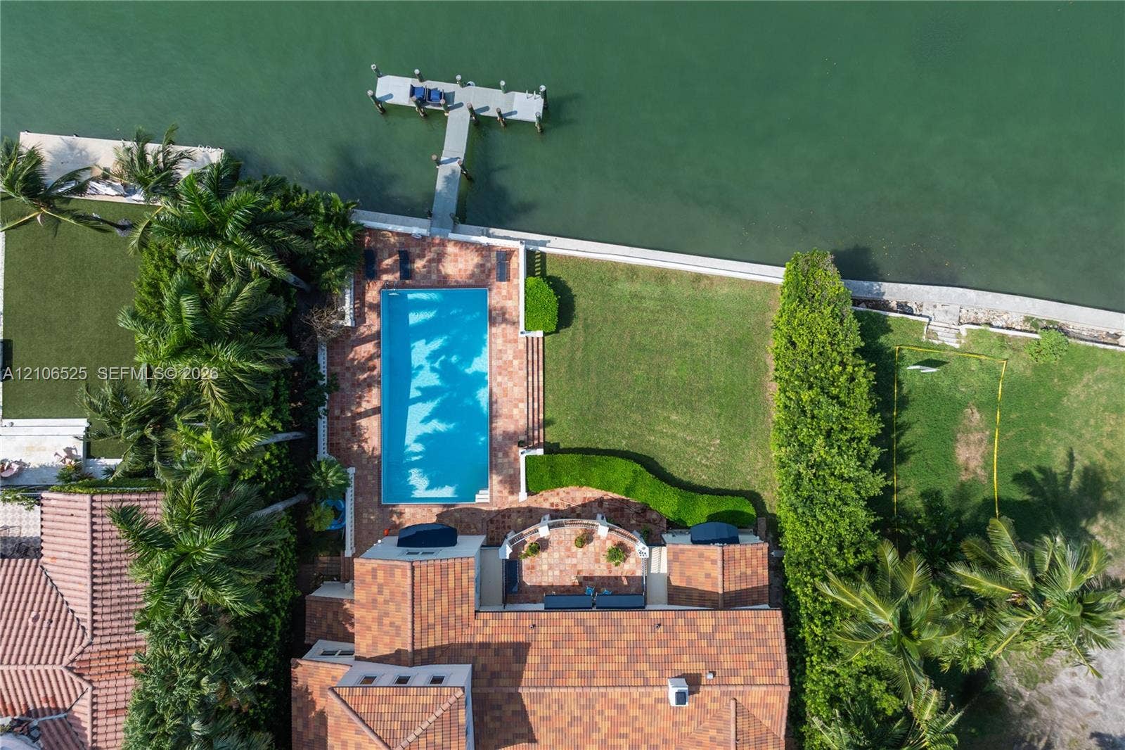 4760 N Bay Road, Miami Beach, FL 33140 Waterfront property featuring a rectangular swimming pool, terracotta-tiled patio, private boat dock, and manicured lawn