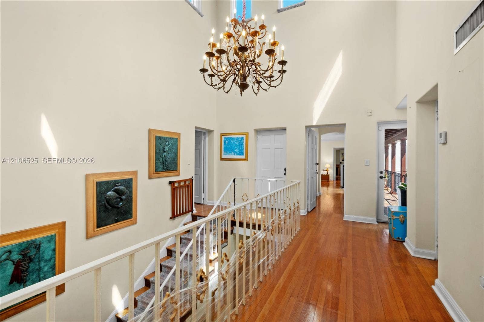 4760 N Bay Road, Miami Beach, FL 33140 Vaulted ceiling featuring a multi-tiered crystal chandelier, wood-finish flooring, and a decorative metal railing