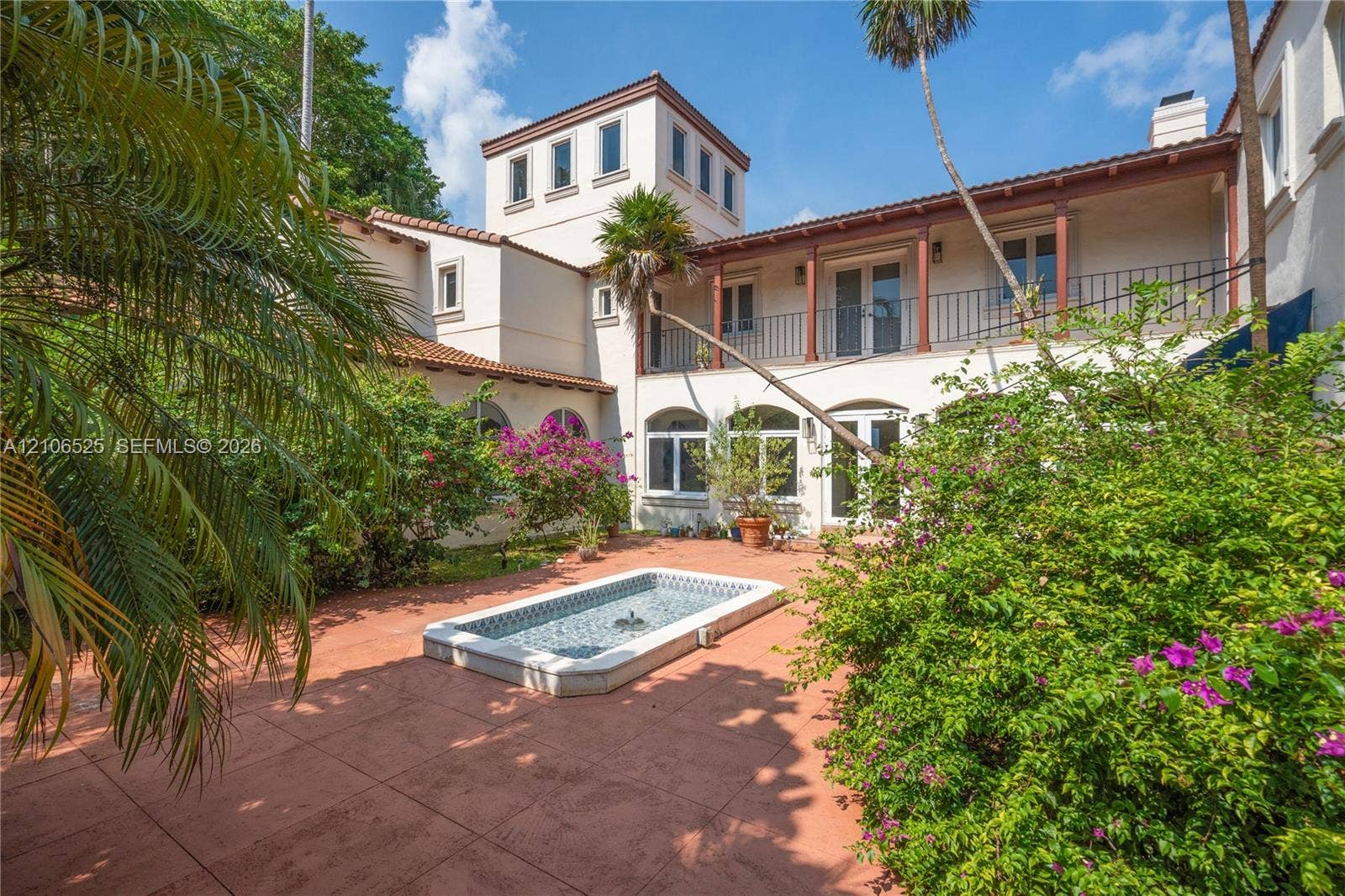 4760 N Bay Road, Miami Beach, FL 33140 Courtyard featuring terra-cotta tile paving, a recessed water feature with decorative tile inlay, a second-story balcony with metal railing, and arched window and door openings