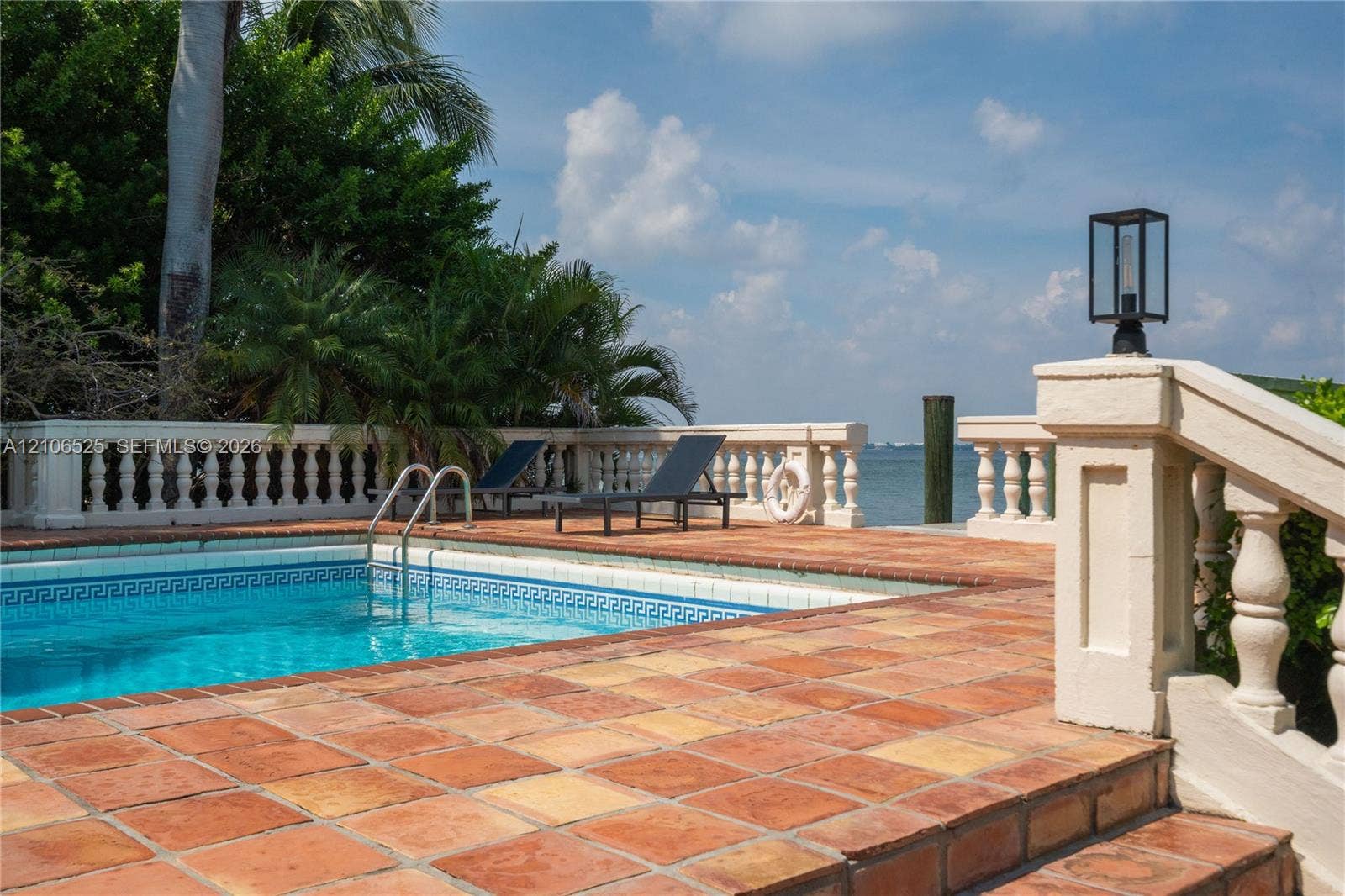 4760 N Bay Road, Miami Beach, FL 33140 Waterfront pool terrace featuring decorative concrete balustrade railings, terracotta tile paving, and built-in lantern-style pillar lighting