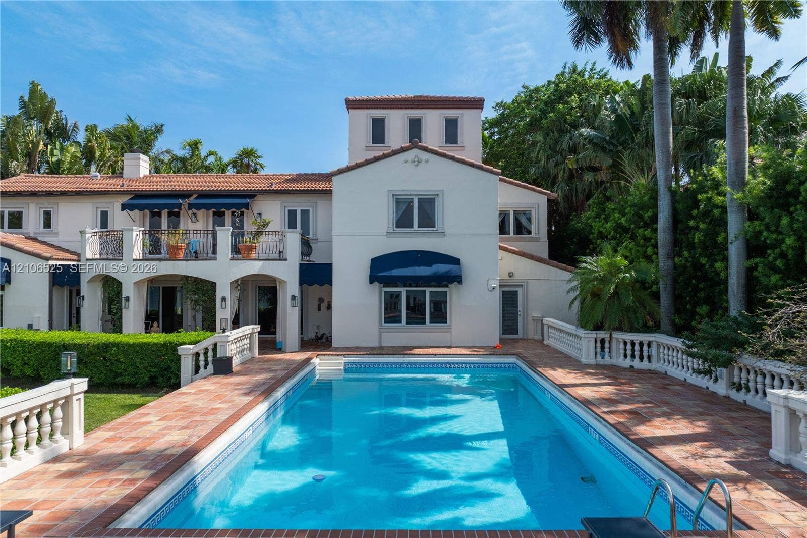 4760 N Bay Road, Miami Beach, FL 33140 Stucco exterior residence featuring a tile roof, second-story balcony, expansive pool area, and classic balustrade hardscaping