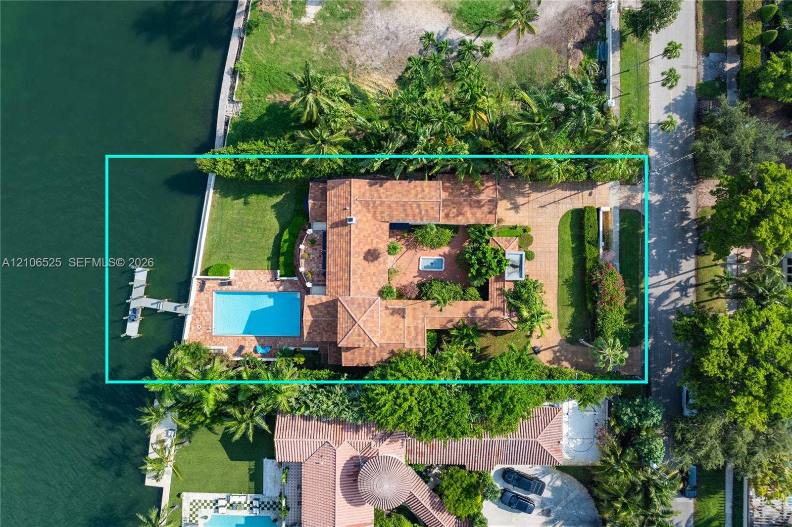 4760 N Bay Road, Miami Beach, FL 33140 Waterfront estate featuring a private dock, rectangular swimming pool, terracotta tile roof, brick-paved courtyard, and mature landscaping