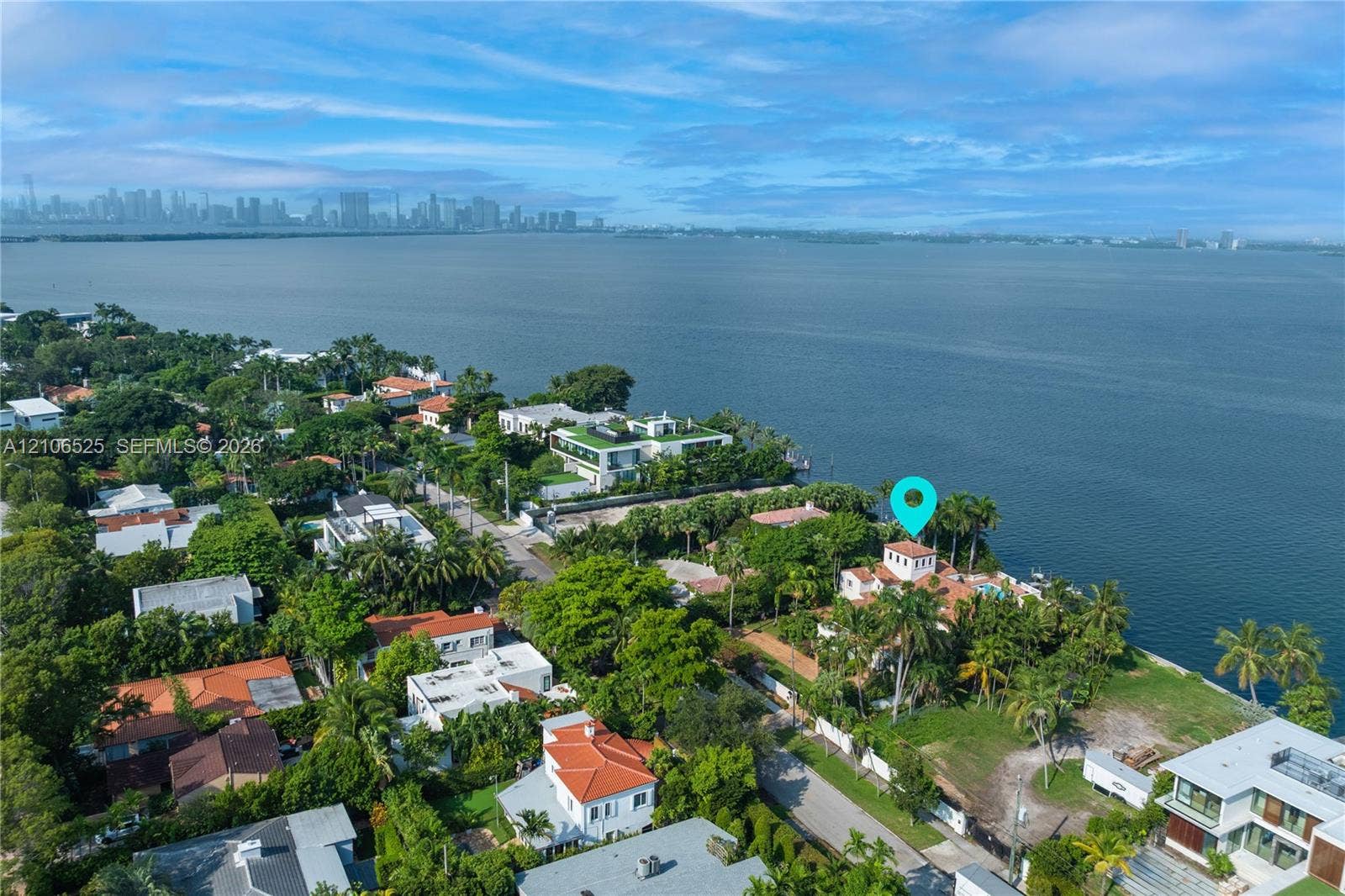 4760 N Bay Road, Miami Beach, FL 33140 Aerial perspective of a waterfront property featuring direct water frontage, a multi-story residence with a red tile roof, and mature perimeter landscaping