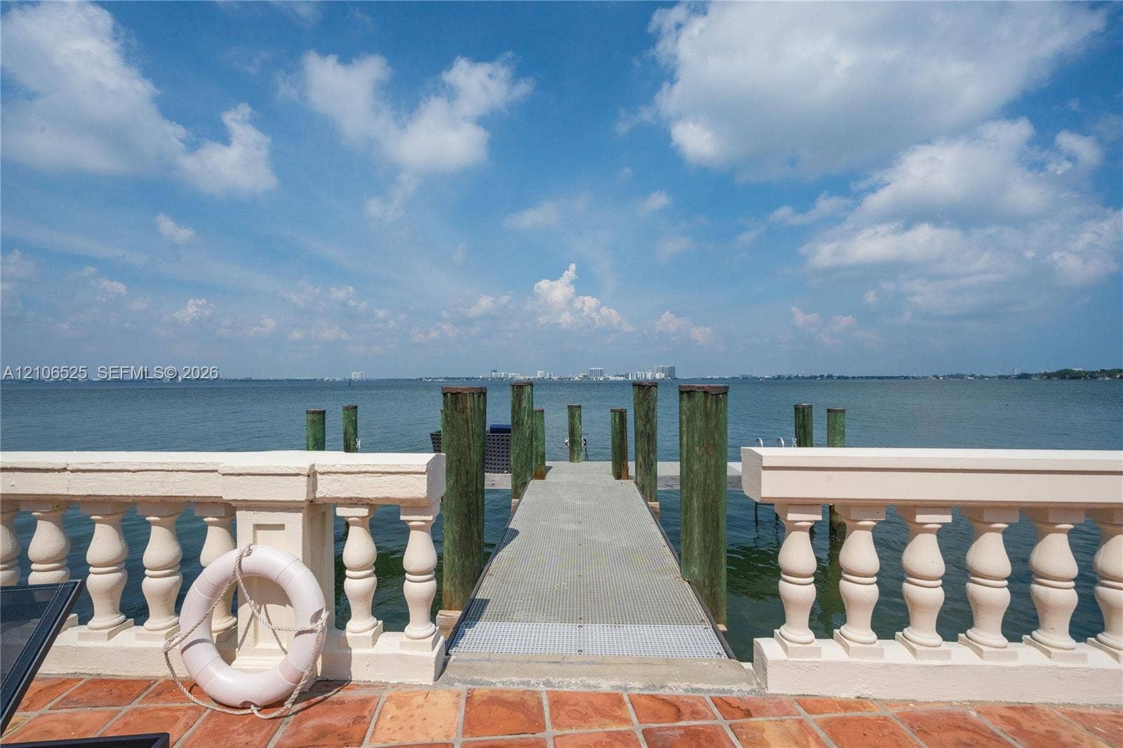 4760 N Bay Road, Miami Beach, FL 33140 Waterfront property featuring a private dock with pilings, stone-paved patio, and classic balustrade railing