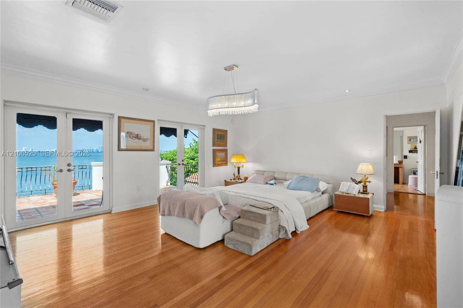 4760 N Bay Road, Miami Beach, FL 33140 Spacious interior featuring wood-finish flooring, dual sets of French doors, crown molding, a decorative crystal chandelier, and a balcony with water scenery