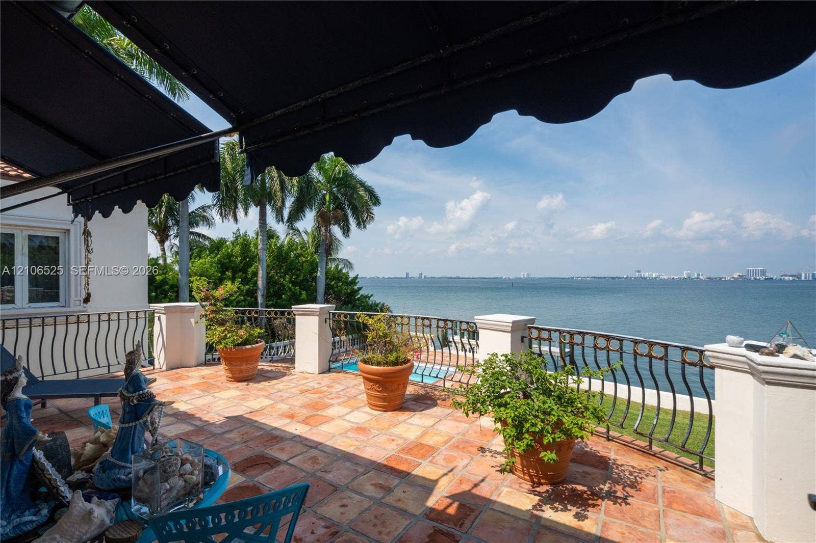 4760 N Bay Road, Miami Beach, FL 33140 Terrace featuring terracotta tile flooring, wrought iron perimeter railing, retractable fabric awning, and masonry pillars