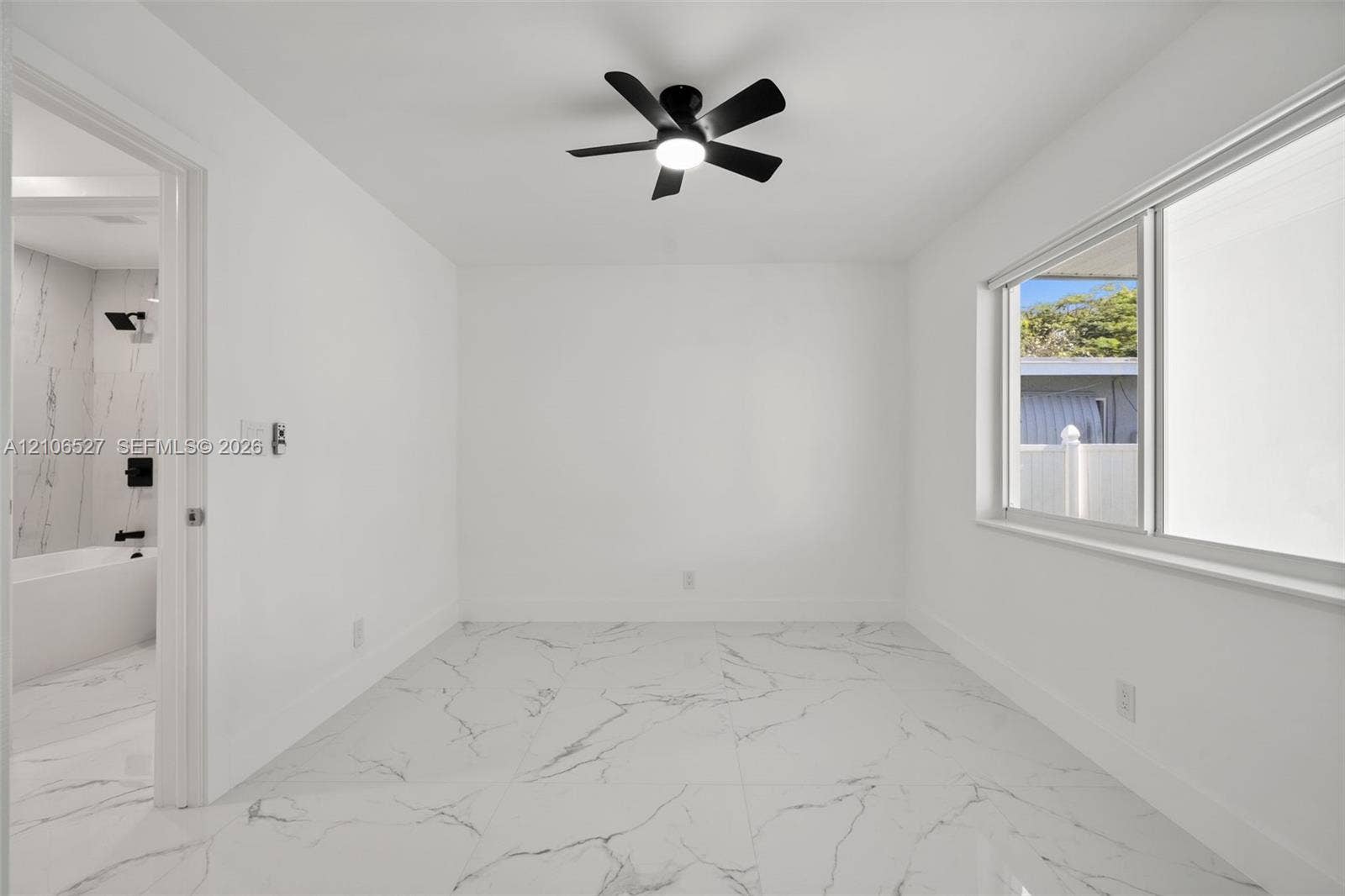 Large-format stone-style tile flooring with veining detail, integrated matte black ceiling fan with light, and wide sliding window