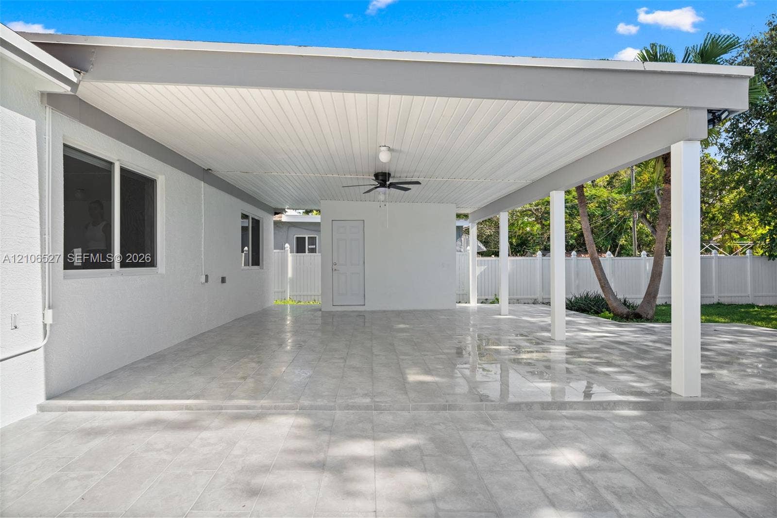 Covered outdoor patio featuring large-format stone-finish tile flooring, beadboard ceiling, ceiling fan, and support columns