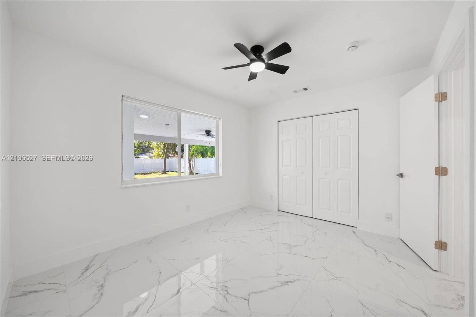 Interior space featuring large-format tile flooring with a neutral veined pattern, dual-panel closet doors, and a matte black ceiling fan with an integrated light fixture