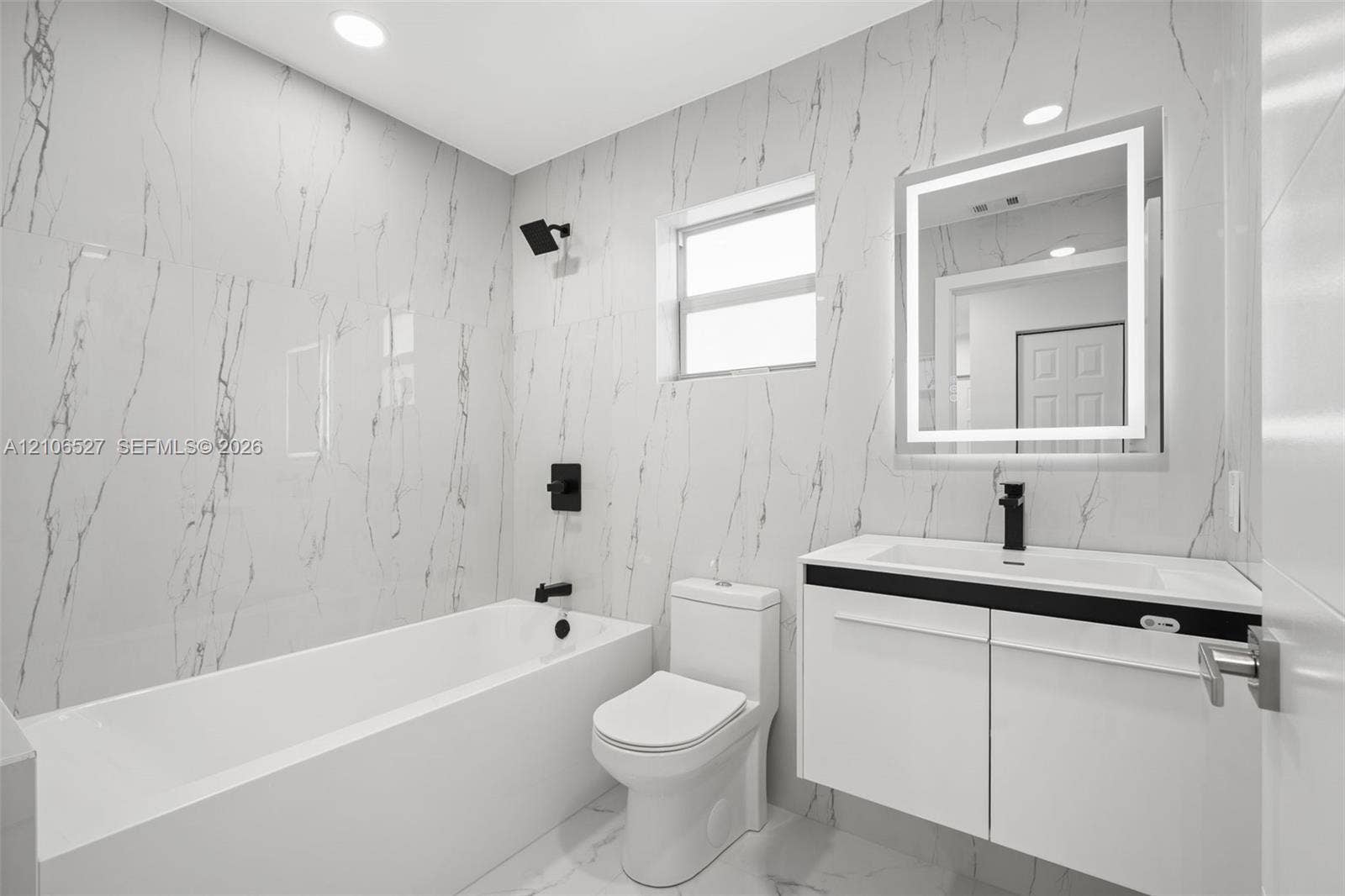 Modern bathroom featuring floor-to-ceiling large-format tile, a floating vanity with a vessel sink, a matte black faucet and shower head, and a built-in LED mirror
