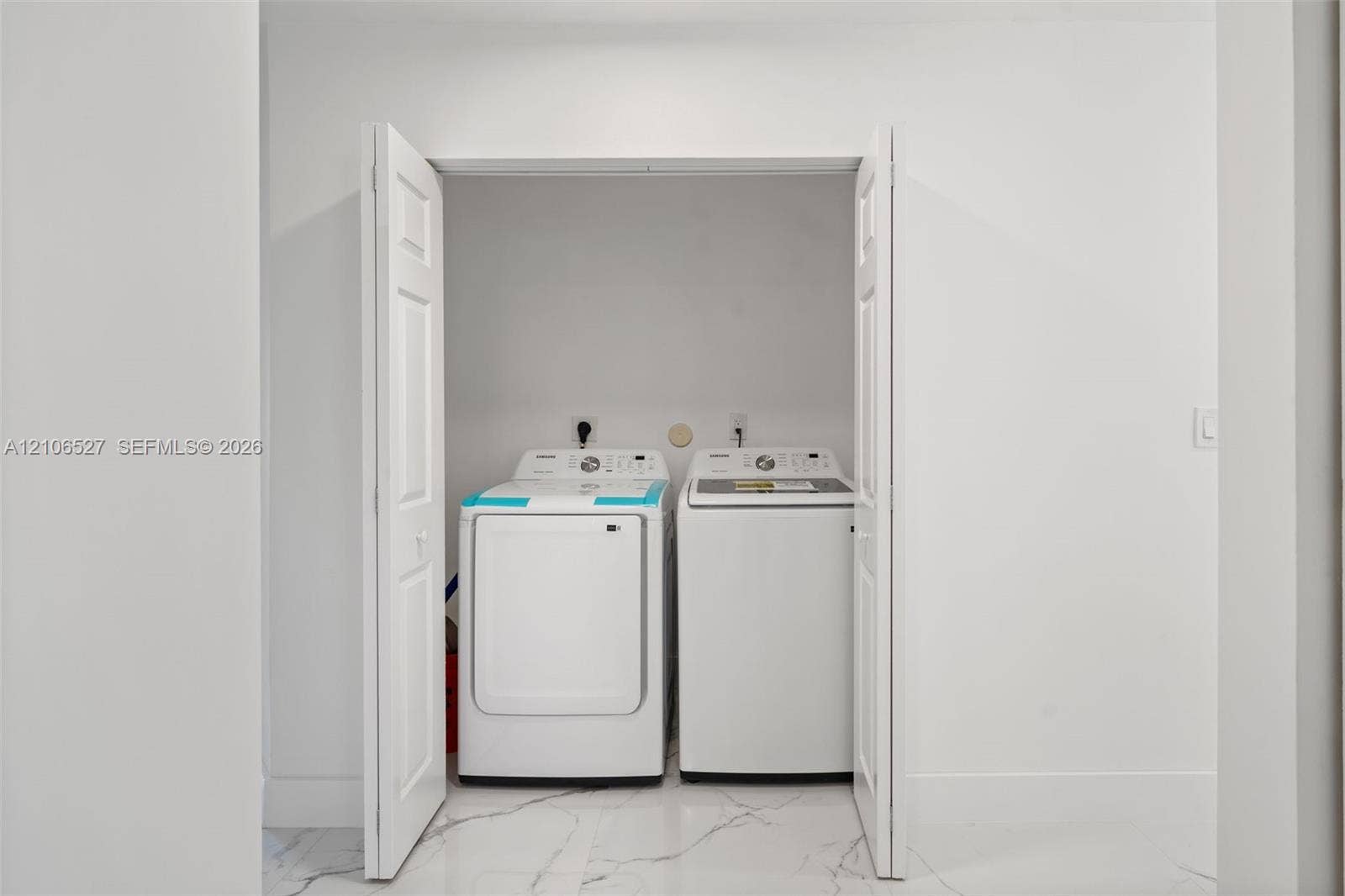 Laundry alcove featuring white bi-fold doors, white interior walls, and tile flooring