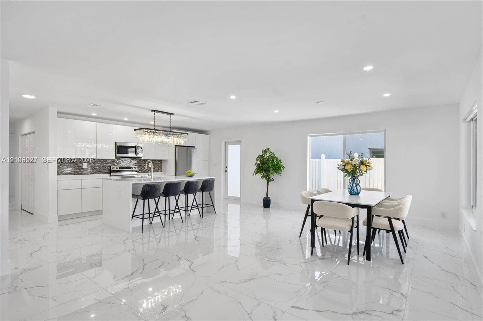 Kitchen featuring white high-gloss cabinetry, stone-finish countertops, stainless steel appliances, a center island with a multi-light pendant fixture, and large-format tile flooring