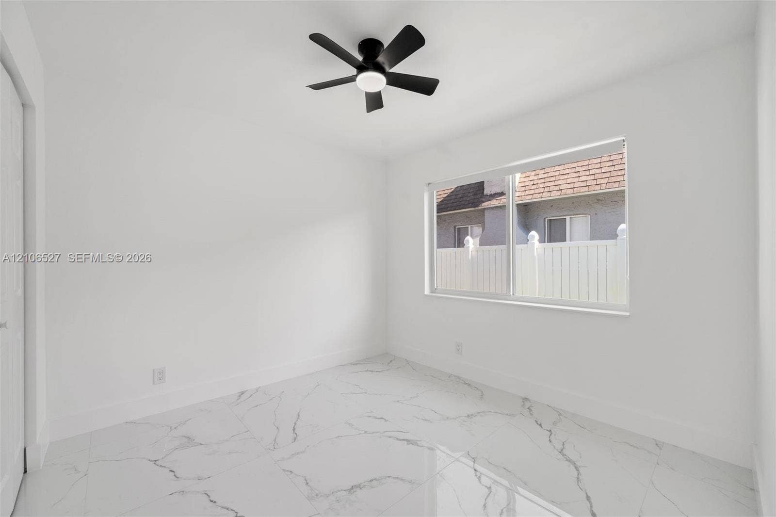 Neutral interior featuring large-format veined tile flooring, a matte black ceiling fan with integrated lighting, and a dual-pane sliding window