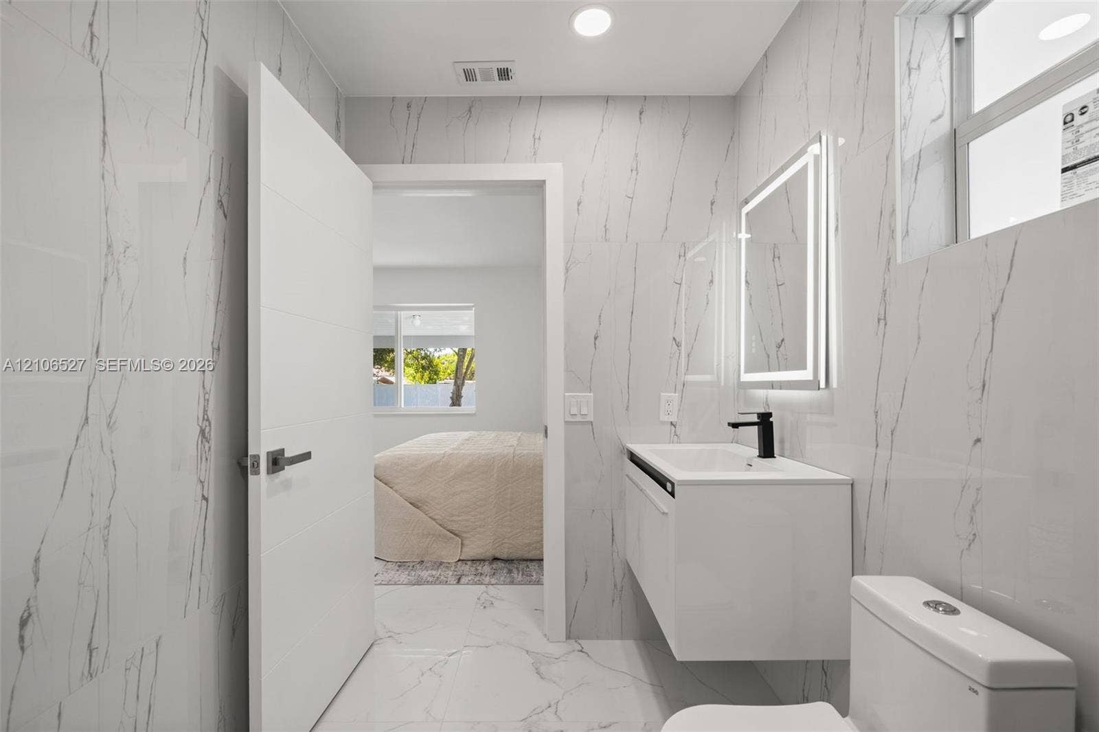 Full-height stone-finish wall tile, floating vanity with an integrated sink, matte black faucet, and backlit LED mirror