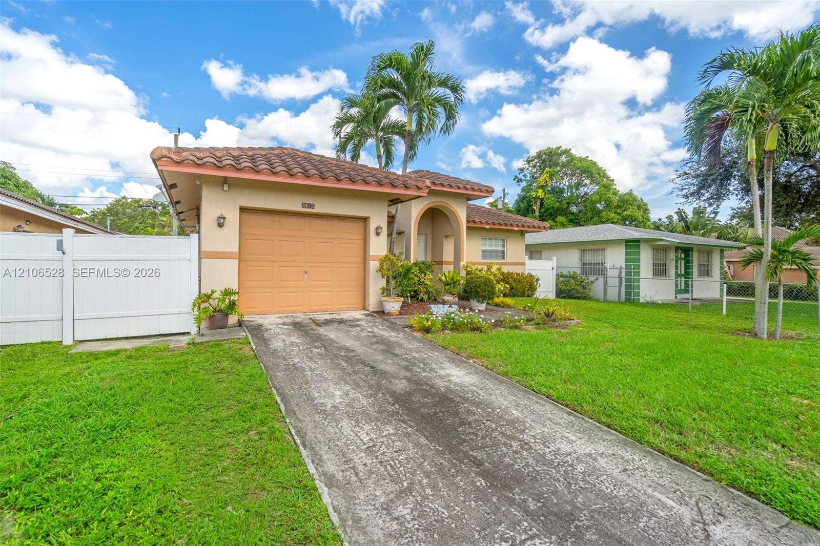 2615 NW 14th Street, Fort Lauderdale, FL 33311 Single-story exterior featuring a clay tile roof, concrete driveway, attached garage, and white vinyl privacy fencing