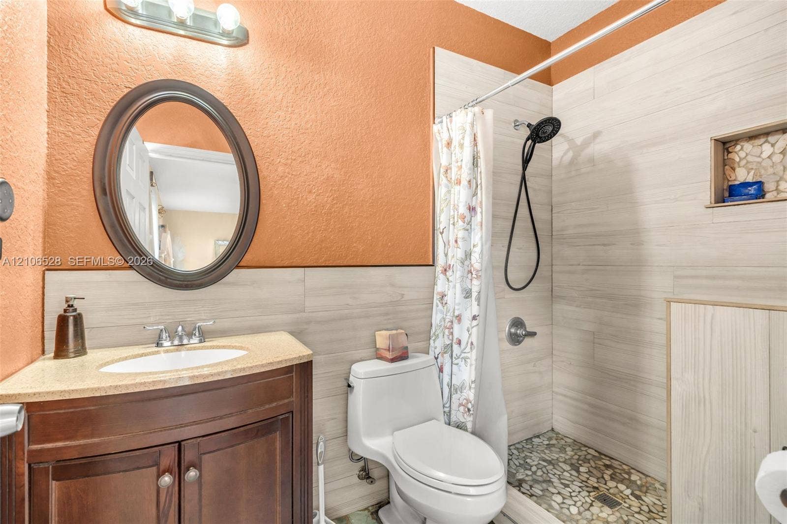2615 NW 14th Street, Fort Lauderdale, FL 33311 Bathroom featuring a wooden vanity with a stone countertop, an oval wall-mounted mirror, wood-finish wall tile, a stone-tiled shower floor, and a built-in shower niche
