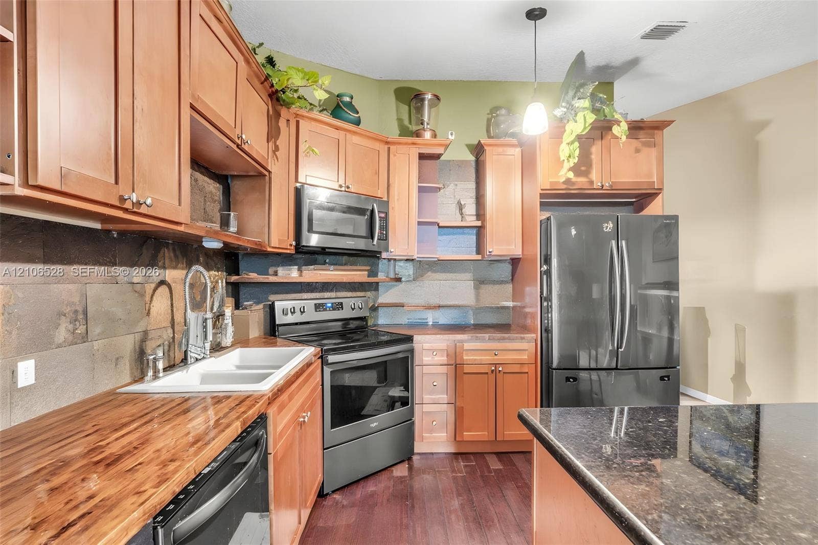 2615 NW 14th Street, Fort Lauderdale, FL 33311 Kitchen featuring wood cabinetry, butcher block countertops, stone-tile backsplash, stainless steel appliances, and a dark stone-surface island