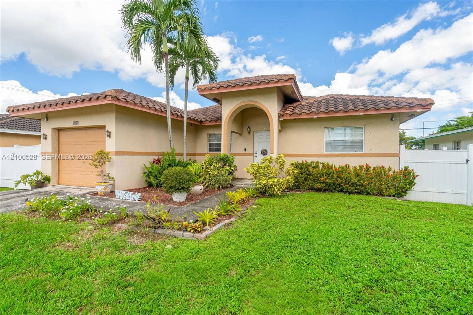 2615 NW 14th Street, Fort Lauderdale, FL 33311 Stucco exterior featuring a terracotta tile roof, arched entryway, single-car garage, and white vinyl privacy fencing