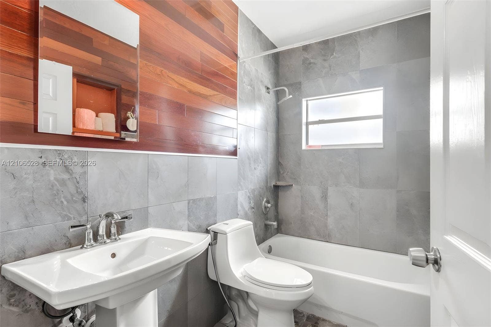 2615 NW 14th Street, Fort Lauderdale, FL 33311 Bathroom featuring gray tile wall surround, horizontal wood-plank accent wall, white pedestal sink with chrome faucet, and integrated shower and tub combination
