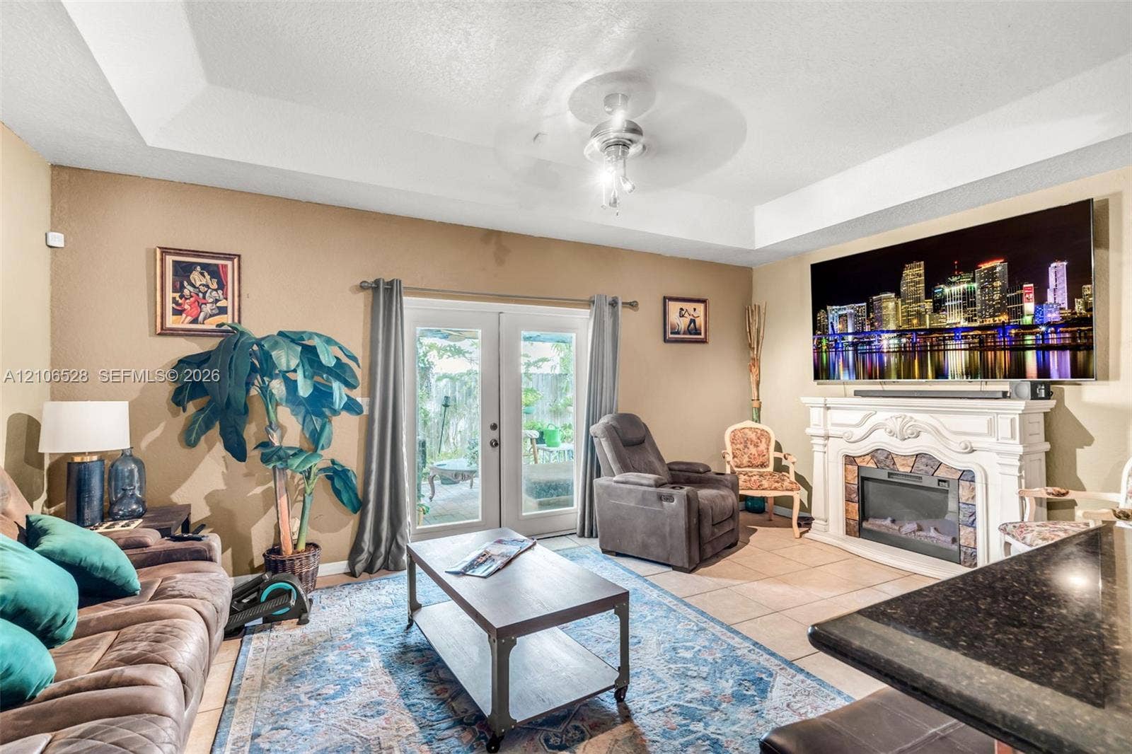 2615 NW 14th Street, Fort Lauderdale, FL 33311 Tray ceiling with central light fixture, fireplace featuring a decorative mantle, and glass-paneled double doors