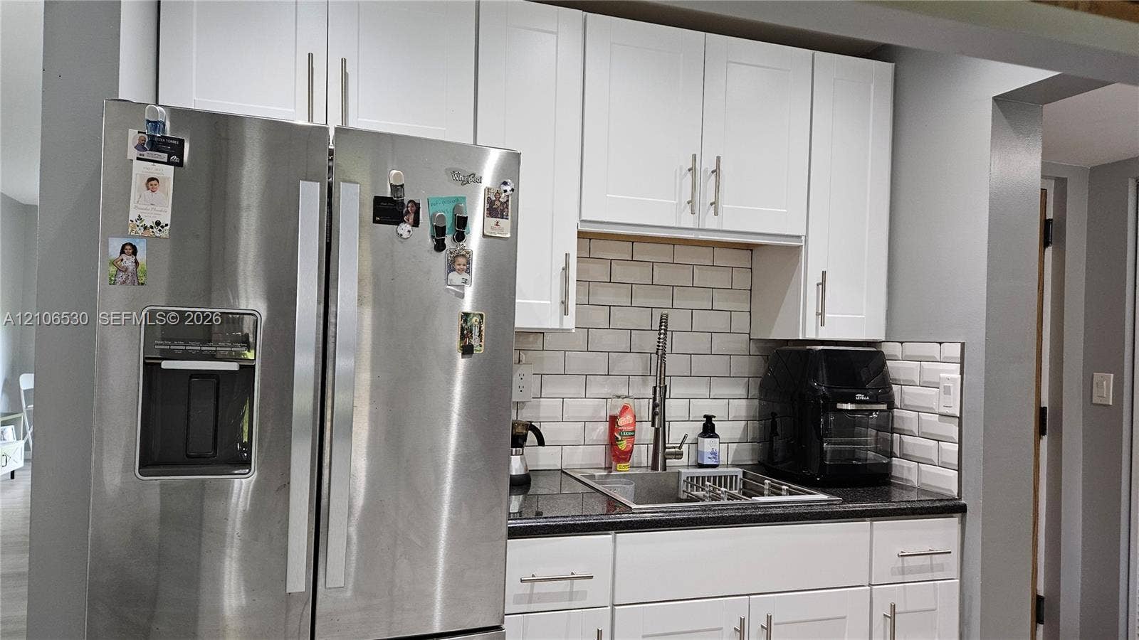 Kitchen area featuring white shaker-style cabinetry, dark countertops, a subway tile backsplash, and a stainless steel side-by-side refrigerator