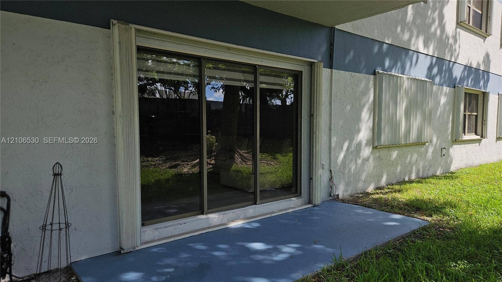 Stucco exterior featuring a sliding glass door, painted concrete patio, and window shutters