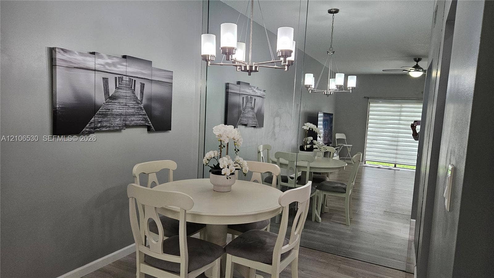 Dining area featuring wood-finish flooring, a full-length wall mirror, a multi-arm chandelier with frosted glass shades, and sliding glass doors
