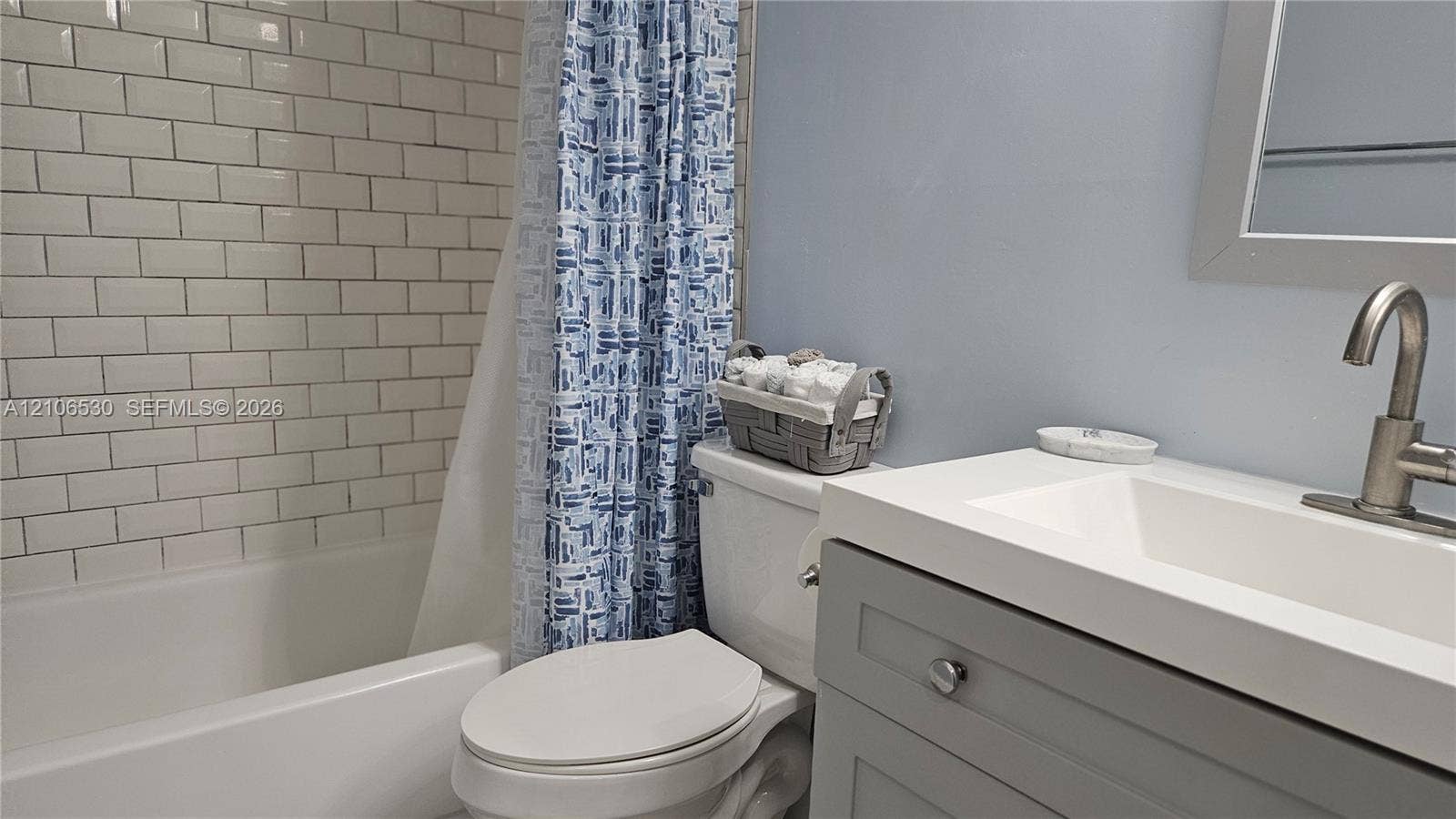 Bathroom featuring a white subway tile shower surround, grey vanity cabinet, white composite countertop with integrated sink, and a brushed nickel finish faucet