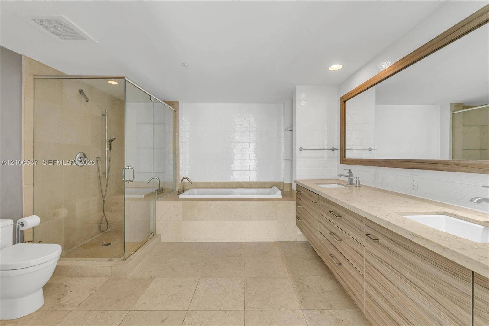 465 Brickell Avenue, #5203, Miami, FL 33131 Bathroom featuring dual-sink vanity with wood-finish cabinetry, stone-style countertop, glass-enclosed shower, and a built-in soaking tub with white tile surround