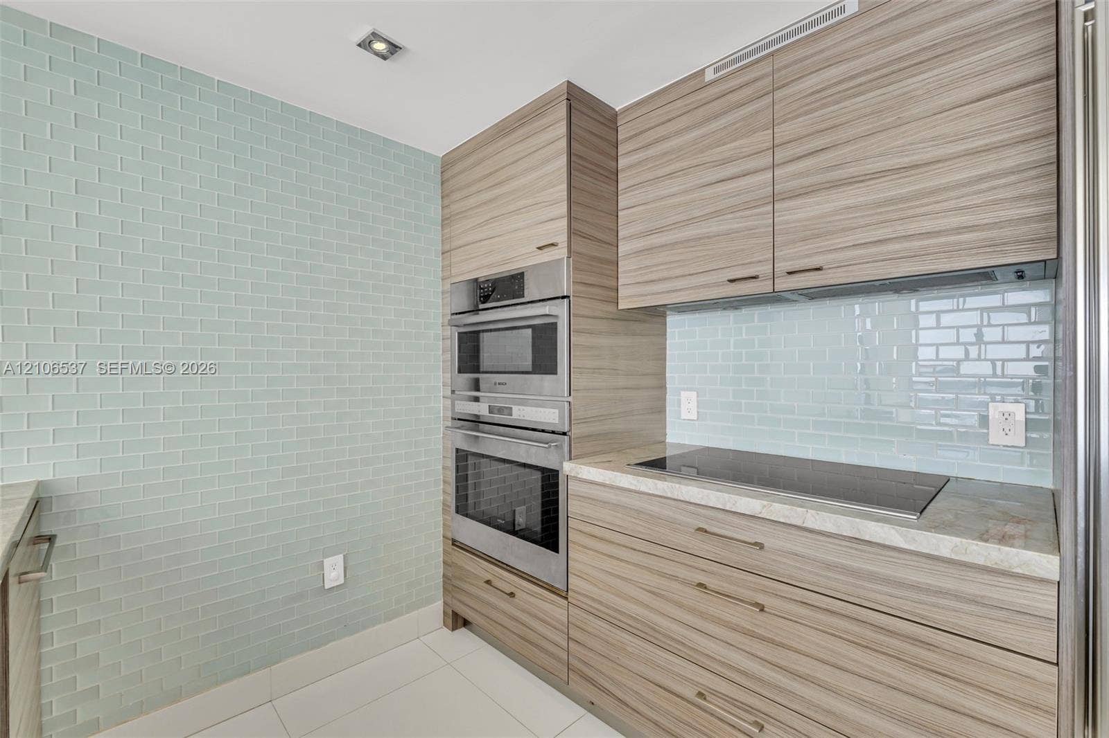 465 Brickell Avenue, #5203, Miami, FL 33131 Modern kitchen featuring wood-finish cabinetry, light blue subway tile backsplash, built-in stainless steel double oven, and integrated cooktop
