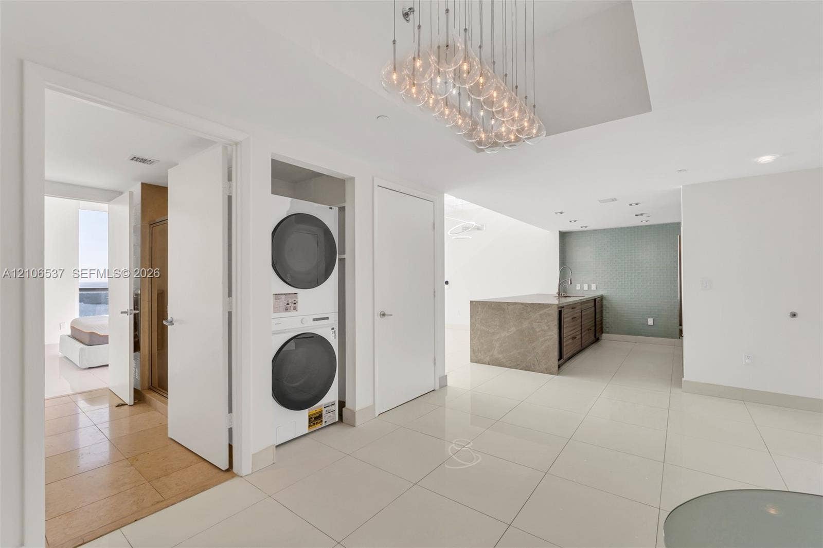 465 Brickell Avenue, #5203, Miami, FL 33131 Large-format polished tile flooring, glass globe chandelier, stacked laundry unit, and kitchen island with stone-finish waterfall countertop