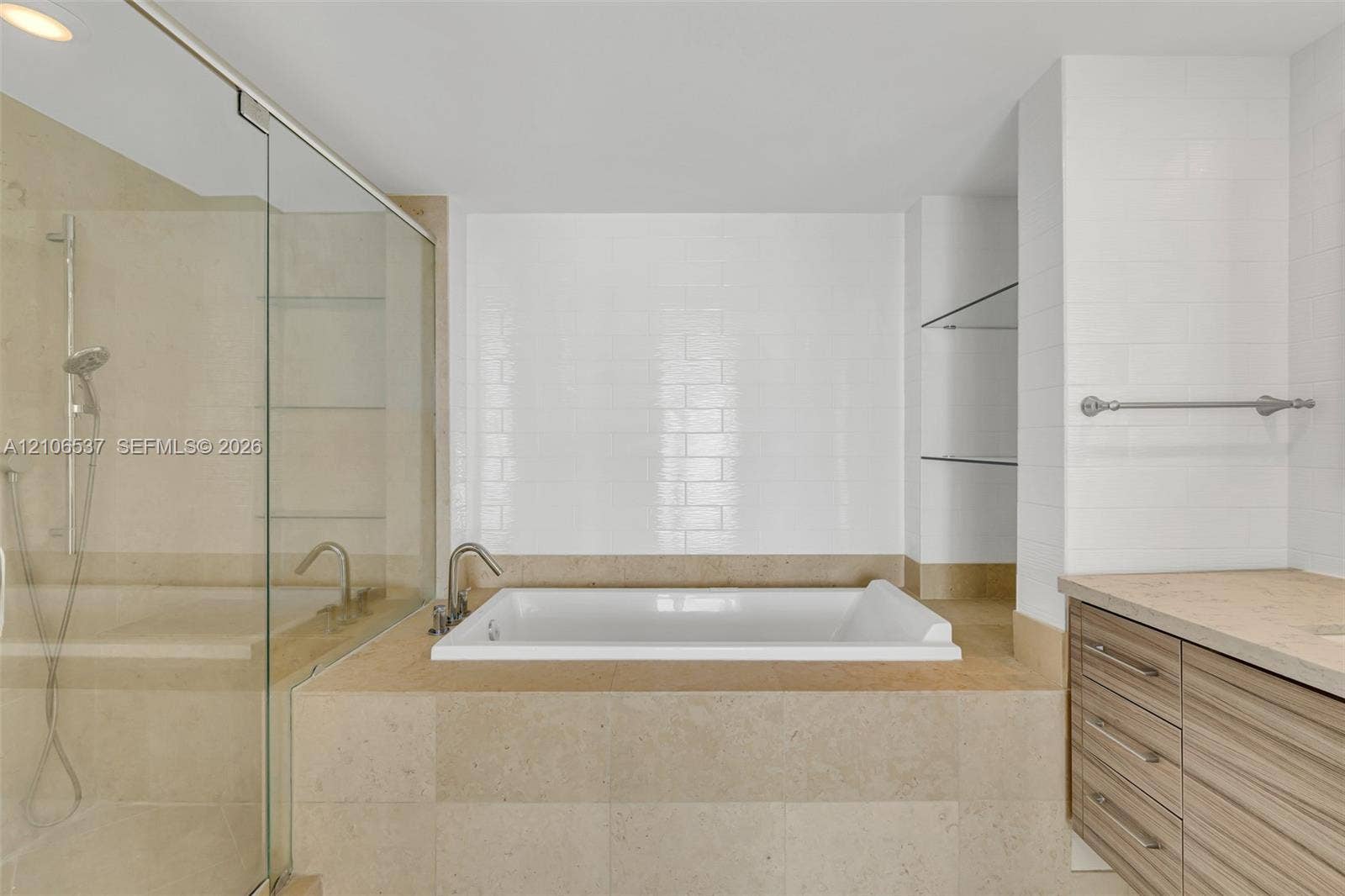 465 Brickell Avenue, #5203, Miami, FL 33131 Soaking tub featuring a tiled surround, glass-enclosed shower, wall-mounted faucet fixtures, wood-finish cabinetry, and built-in glass shelving