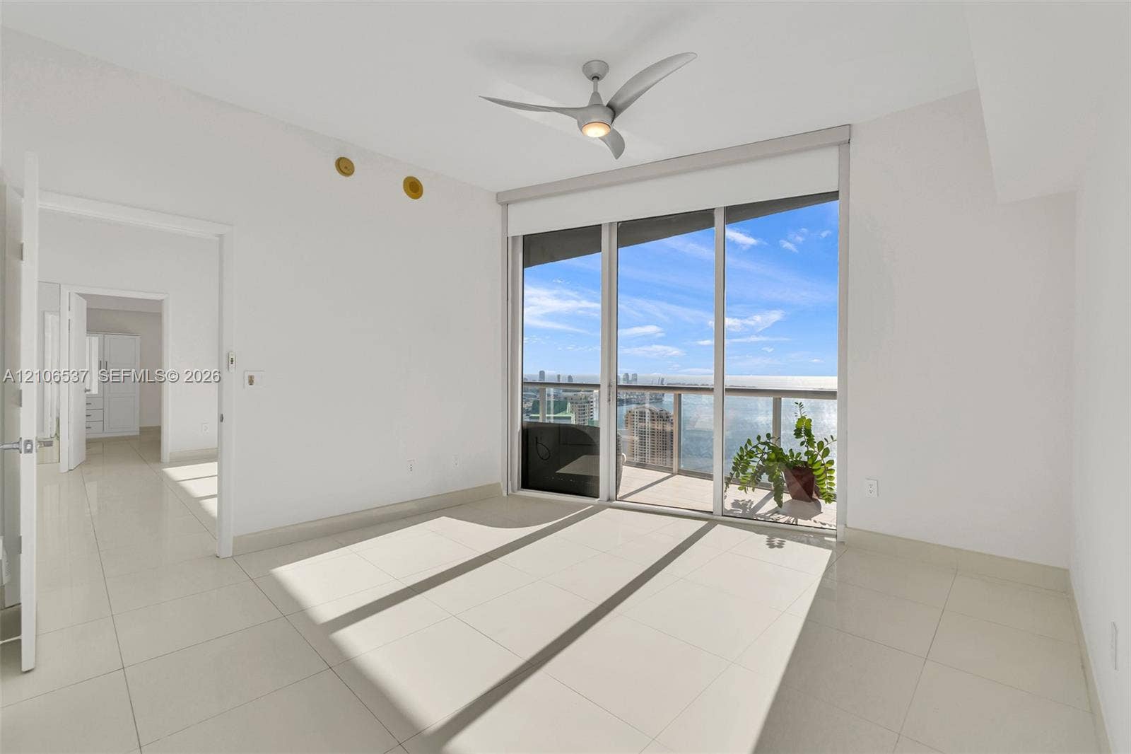 465 Brickell Avenue, #5203, Miami, FL 33131 Floor-to-ceiling glass sliding doors opening to a private balcony, polished tile flooring, three-blade ceiling fan with integrated lighting, and panoramic water and city skyline outlooks