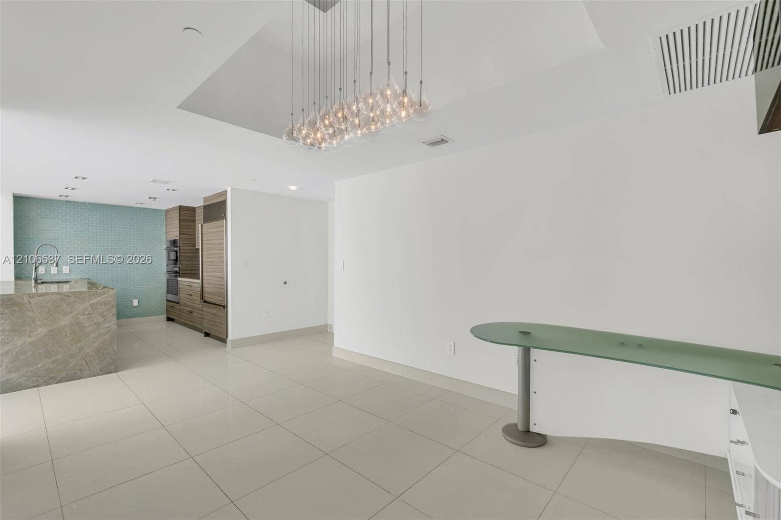 465 Brickell Avenue, #5203, Miami, FL 33131 Large-format tile flooring, multi-pendant glass chandelier, built-in stone-surfaced kitchen island, wall-mounted curved glass console, and floor-to-ceiling wooden cabinetry with integrated appliances