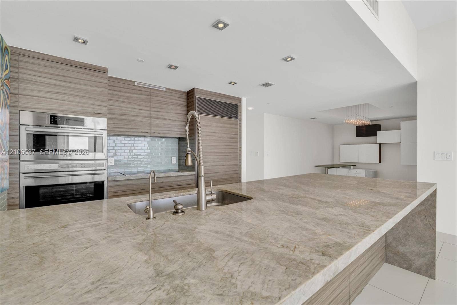 465 Brickell Avenue, #5203, Miami, FL 33131 Kitchen featuring a waterfall-edge stone countertop, wood-finish cabinetry, stainless steel built-in double wall oven, recessed lighting, and a dual-basin stainless steel sink with a high-arch faucet