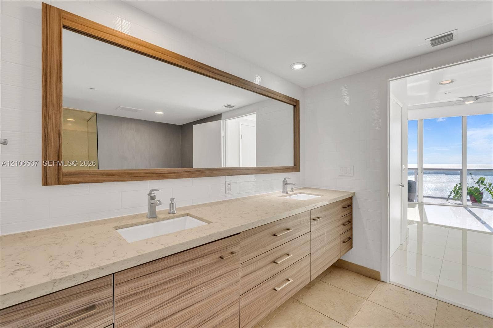 465 Brickell Avenue, #5203, Miami, FL 33131 Dual-sink floating vanity with wood-finish cabinetry, stone countertop, integrated rectangular sinks, and an oversized wood-framed mirror