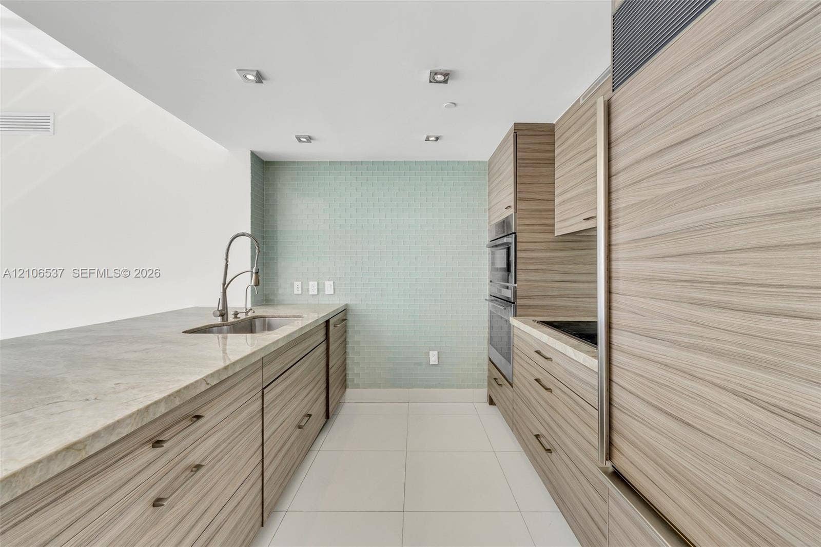 465 Brickell Avenue, #5203, Miami, FL 33131 Kitchen featuring horizontal wood-grain cabinetry, stone countertops, integrated stainless steel appliances, a tile backsplash, and recessed lighting