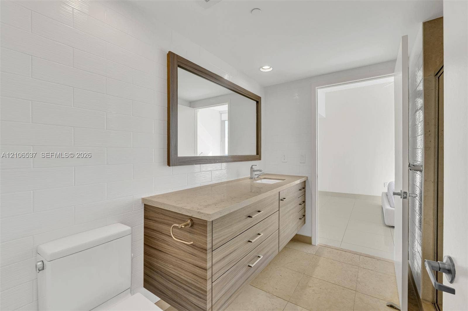 465 Brickell Avenue, #5203, Miami, FL 33131 Floating vanity with wood-finish cabinetry, stone countertop, integrated sink, framed wall mirror, and subway-tiled wall