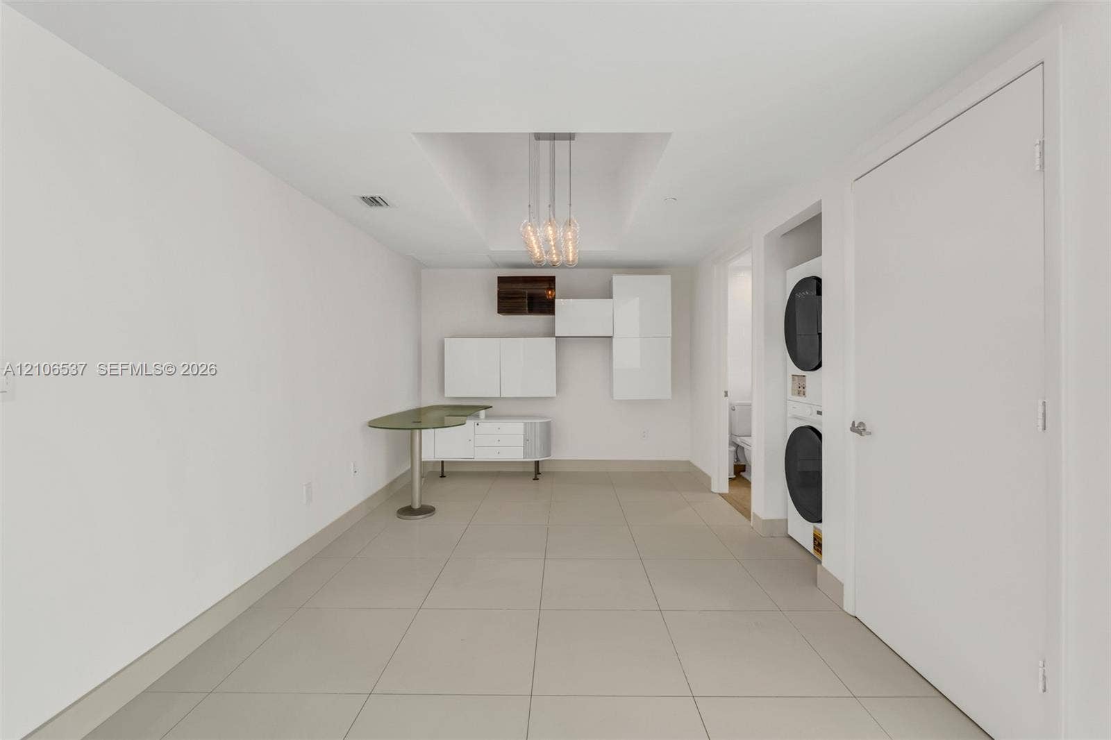 465 Brickell Avenue, #5203, Miami, FL 33131 Modern utility space featuring large-format tile flooring, built-in glossy white cabinetry, an integrated stone-surface workstation, a tiered pendant light fixture, and a stacked washer and dryer unit
