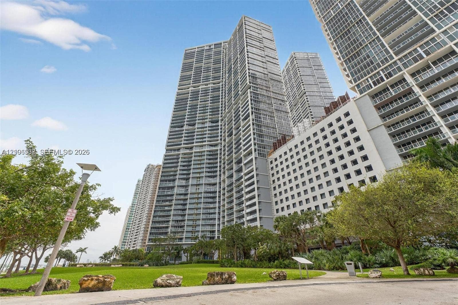 465 Brickell Avenue, #5203, Miami, FL 33131 High-rise glass and concrete tower featuring tiered balconies, floor-to-ceiling windows, an expansive manicured lawn, and lush mature trees