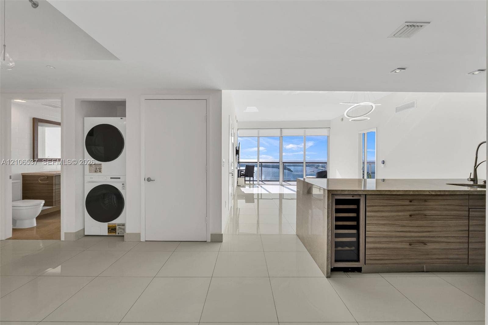 465 Brickell Avenue, #5203, Miami, FL 33131 Open-concept interior featuring large-format tile flooring, stacked laundry unit, built-in wine cooler, wood-finish cabinetry, and floor-to-ceiling windows