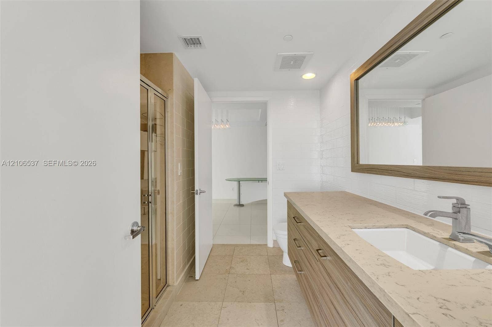 465 Brickell Avenue, #5203, Miami, FL 33131 Bathroom vanity with neutral stone-style countertop, wood-finish cabinetry, rectangular undermount sink, and full-width framed mirror, complemented by a glass-enclosed shower featuring textured tile surround