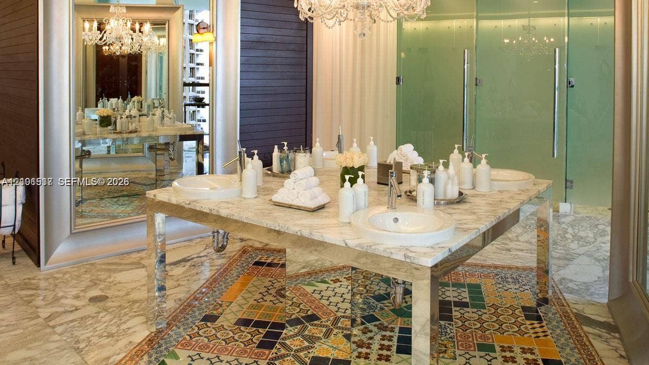 465 Brickell Avenue, #5203, Miami, FL 33131 Custom vanity featuring a natural stone countertop, dual undermount sinks, and polished metal legs, complemented by decorative geometric tile flooring and a large-scale crystal chandelier