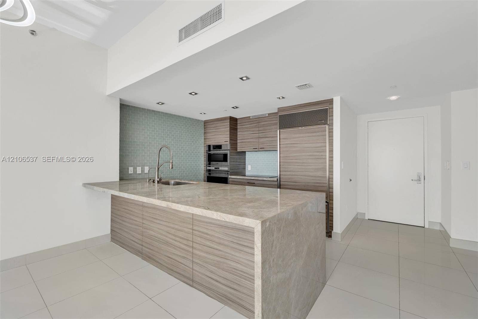 465 Brickell Avenue, #5203, Miami, FL 33131 Kitchen featuring a waterfall-edge stone countertop, wood-finish cabinetry, built-in stainless steel refrigerator, recessed lighting, and patterned tile backsplash
